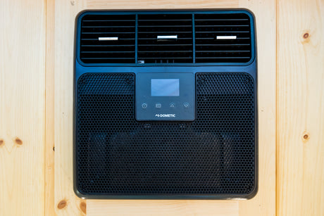 Black Dometic RV air conditioner unit with display panel and vents, mounted on wood, perfect for your rv rental comfort.