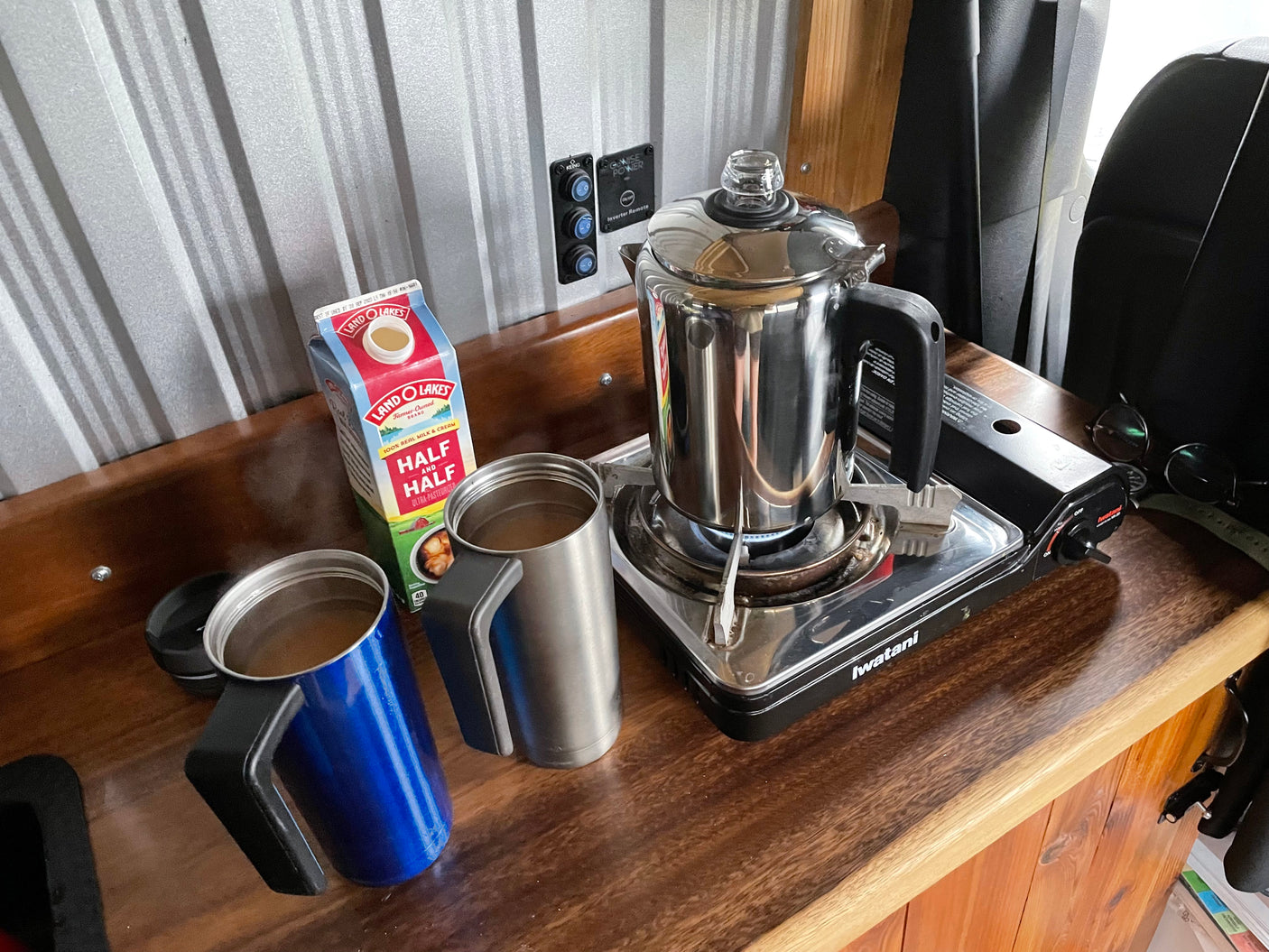 Morning coffee setup in an RV rental: percolator brewing on a portable stove, with mugs and half & half ready.
