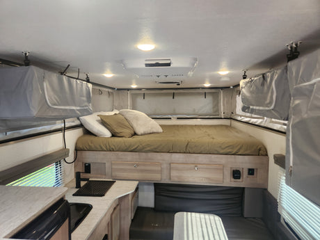 Spacious pop-up camper interior for RV rental. Features a large bed, kitchen, and dining area with blinds.