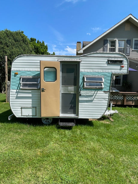 Vintage light blue camper parked on green grass, with a house in the background. Great for an RV rental!
