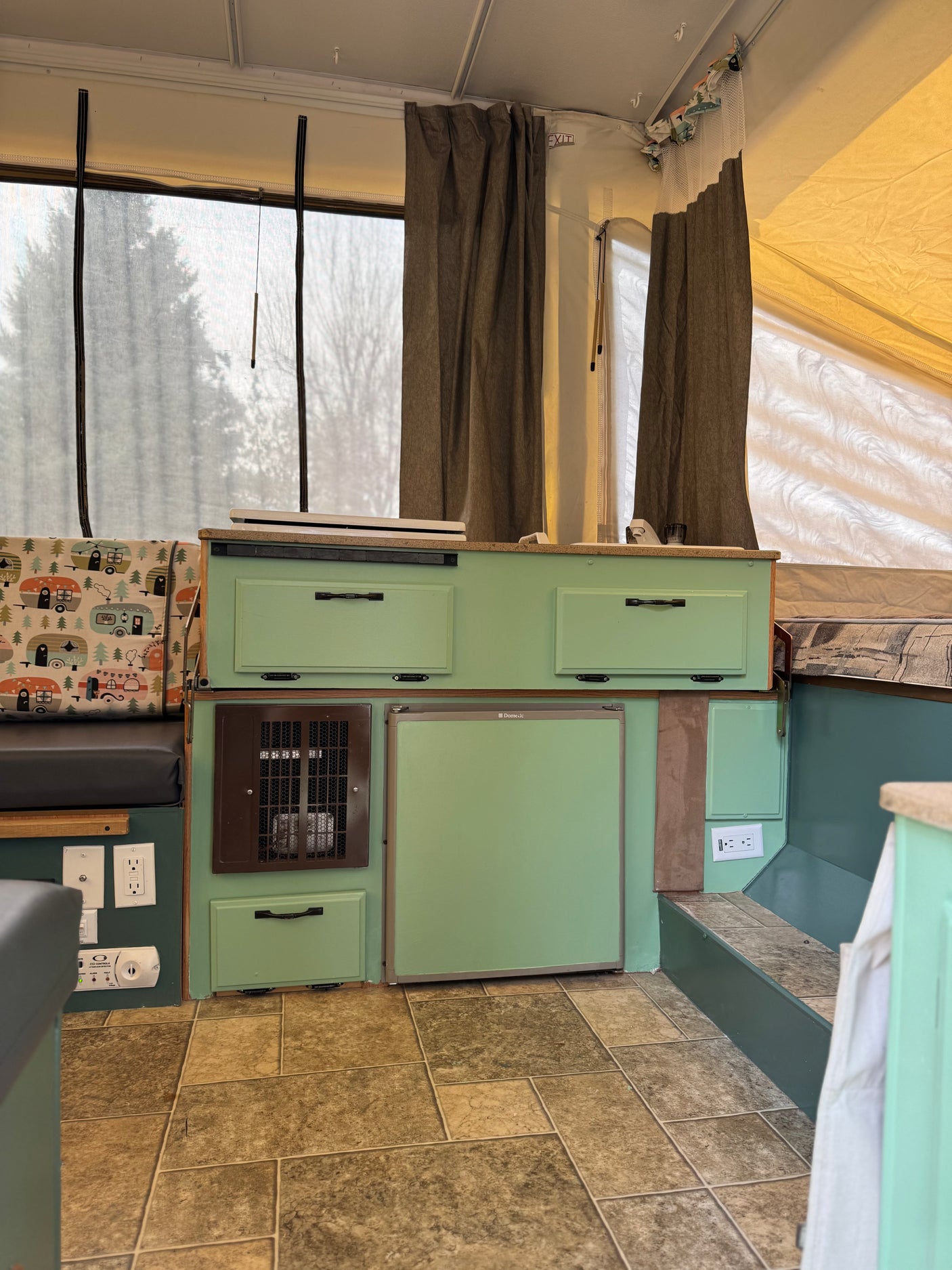 Explore this cozy RV rental pop-up camper interior with custom light green cabinets, fridge, and fun patterned cushion.