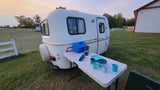 Cozy RV rental camper with outdoor dining setup and blue dishes on a folding table in a grassy field.