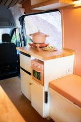 RV rental kitchen: a chic salmon-pink pot on an induction cooktop, oven, fridge, and cozy bench. Van life essentials.