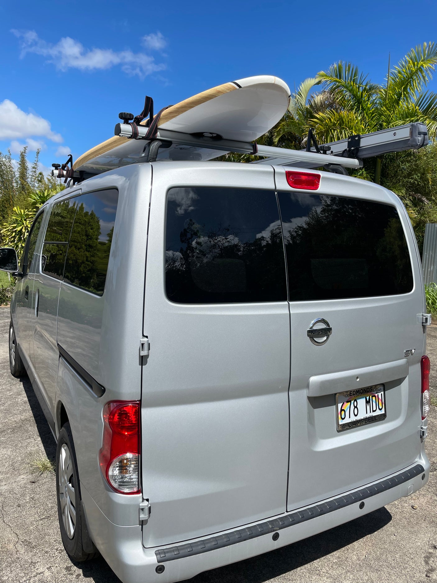 Silver Nissan NV200 van, a versatile RV rental option, with a surfboard ready for beach adventures.