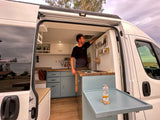 Enjoy mobile comfort in this RV rental! Man in a custom camper van kitchen, featuring a smart pull-out table.