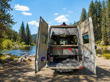 RV rental camper van with open rear doors, revealing storage, parked by a scenic river for forest adventures.