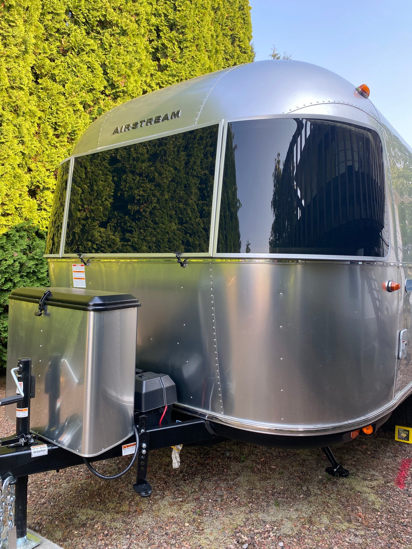 Front view of a sleek Airstream travel trailer, great for an rv rental. Its polished surface reflects green trees and buildings.