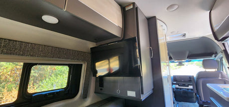 Inside a modern RV rental, featuring a mounted TV, ample overhead storage, and a large window overlooking nature.