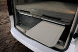 Inside an RV rental: a compact, modular bed with "Caravan Master" branding, and a grey pull-out table extended from beneath.
