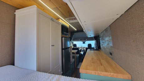 Spacious rv rental interior: a comfy bed, kitchenette with fridge & microwave, and front cab visible in this modern camper van.