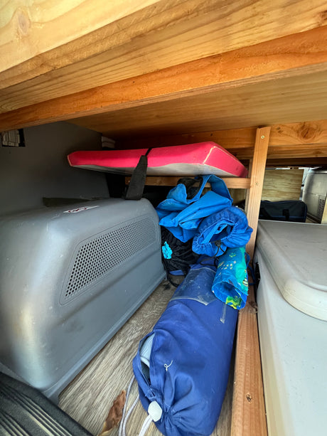 RV rental's organized under-bed storage, featuring a portable fridge, sleeping pad, and blue travel gear.