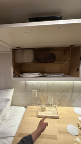 Organized RV rental interior featuring overhead storage with plates & counter with drinks, ideal for compact living.