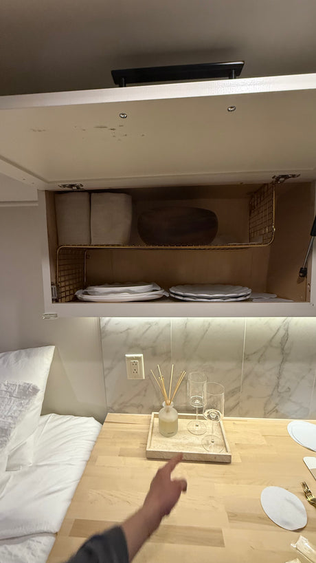 Organized RV rental interior featuring overhead storage with plates & counter with drinks, ideal for compact living.