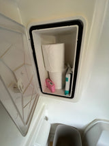 Open RV rental storage with toilet paper, a pink box, and a teal package. Essential compact bathroom supplies.