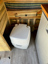RV rental interior: A portable toilet, wooden walls, and striped bedding in a compact space.