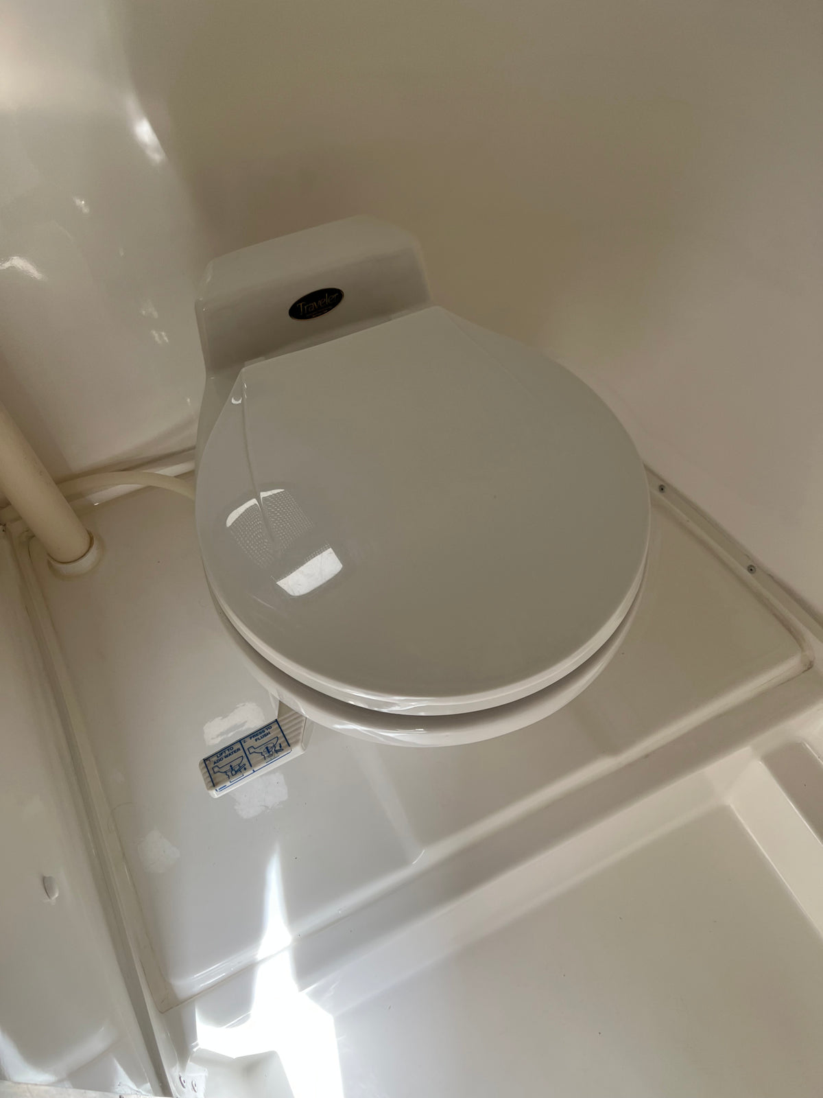 White Traveler RV rental toilet with lid closed. Visible flush instructions (lift to add water, press to flush) are on the base. — photo 2