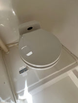 White Traveler RV rental toilet with lid closed. Visible flush instructions (lift to add water, press to flush) are on the base.