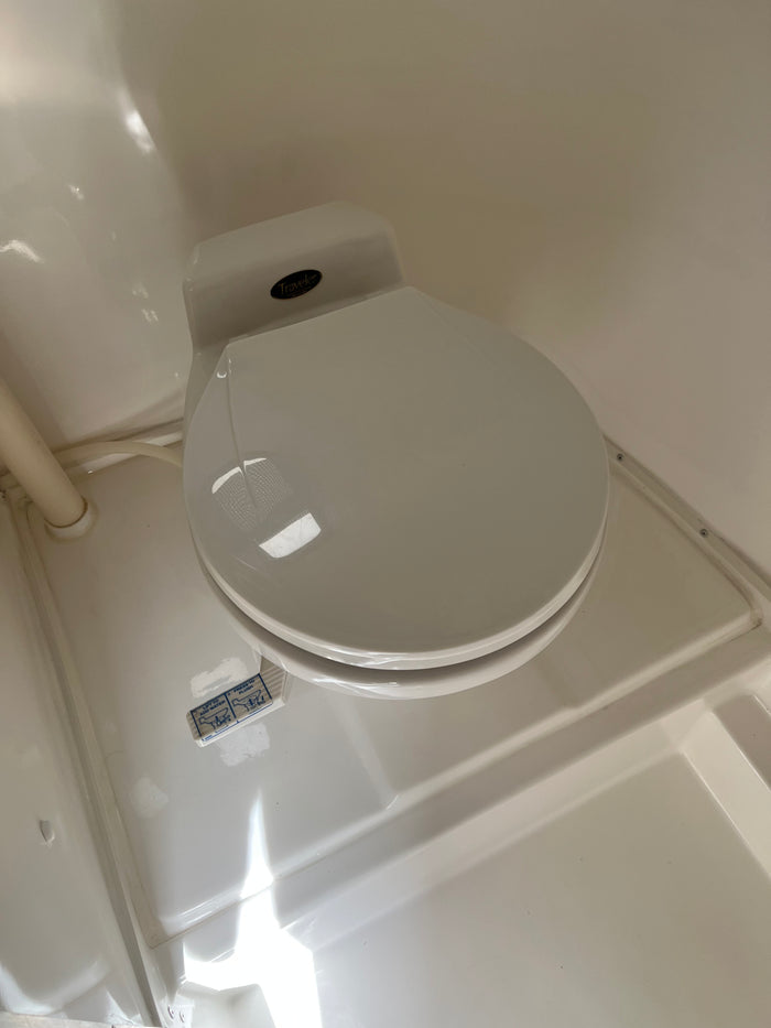 White Traveler RV rental toilet with lid closed. Visible flush instructions (lift to add water, press to flush) are on the base.