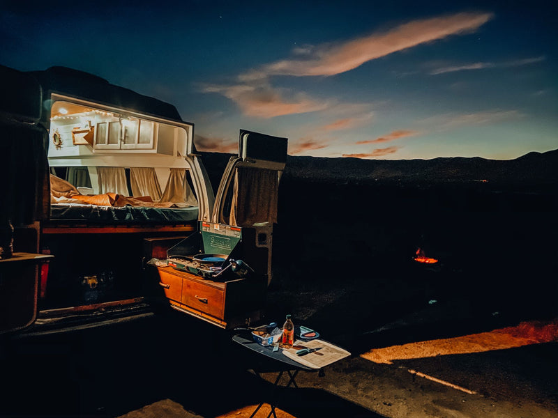 An RV rental glowing at dusk, with its cozy interior, an outdoor kitchen, and a distant campfire under a starry sky. — photo 14