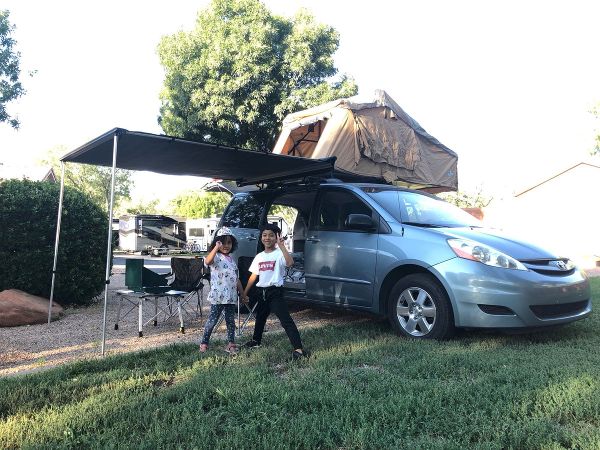  E-Bikes Available.|Two kids with their RV rental setup: a minivan with a rooftop tent and awning at a campground