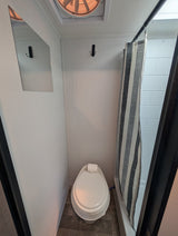 A compact RV rental wet bath with a toilet, striped shower curtain, wall mirror, and ceiling fan.