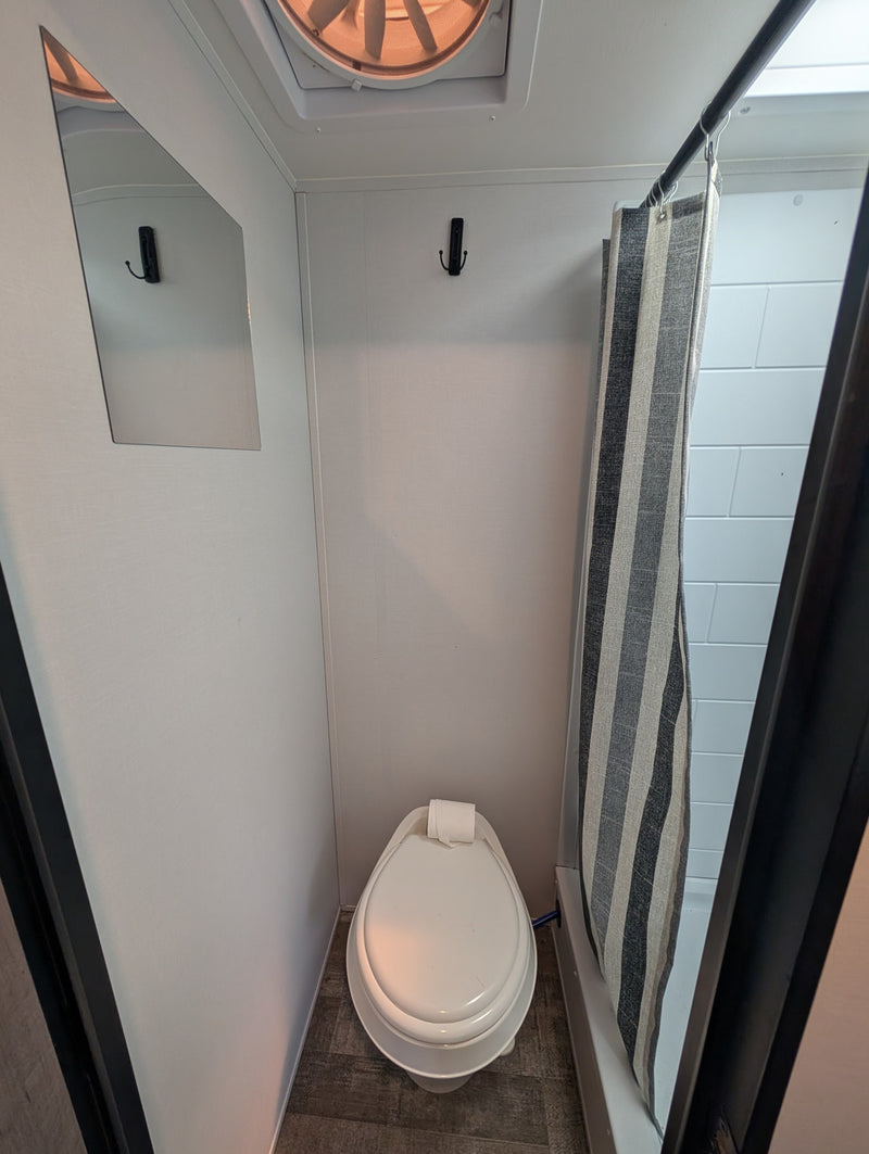 A compact RV rental wet bath with a toilet, striped shower curtain, wall mirror, and ceiling fan. — photo 5