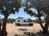 A white camper van, ideal as an rv rental, is parked in a dry, scenic landscape, framed by majestic trees.