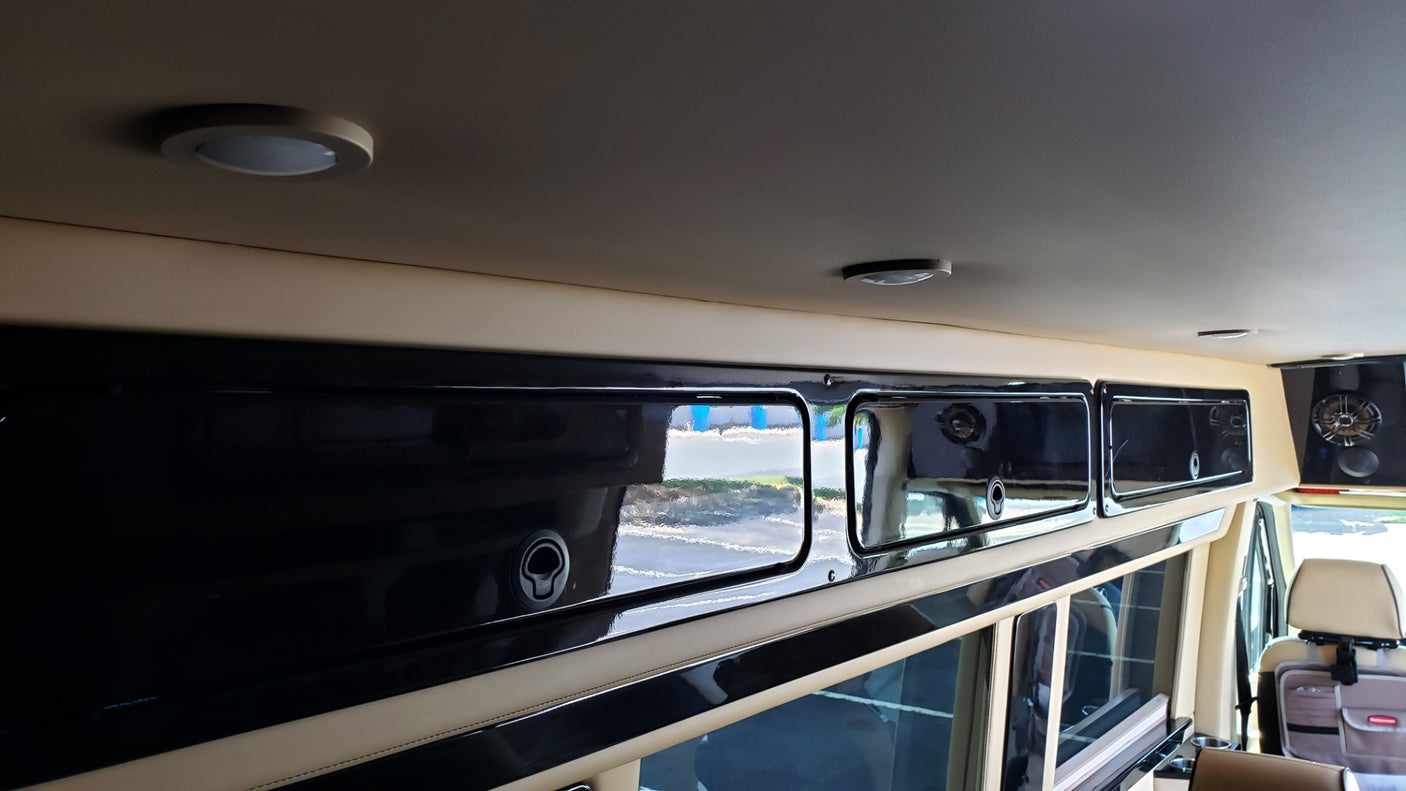 Inside an RV rental: view of custom black overhead cabinets, beige paneling, and ceiling lights. Spacious and modern.