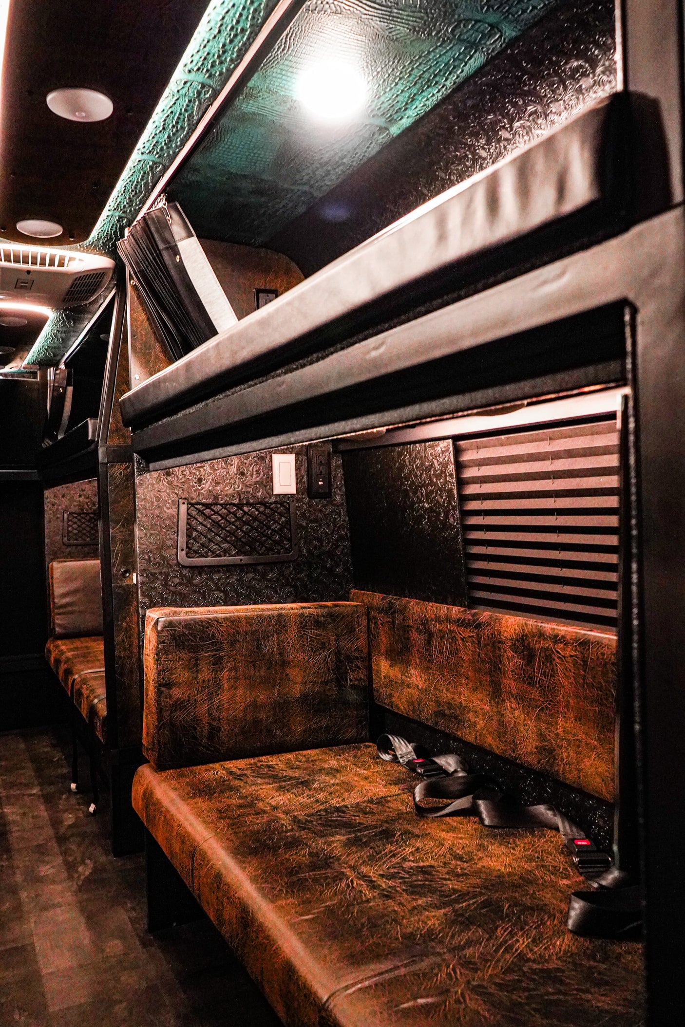 Luxurious custom RV rental interior with distressed brown seating, textured walls, and overhead bunks.