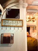 This RV rental interior features decorative signs, a pressed botanical frame with hooks, and a mesh basket, leading to the cozy bedroom.