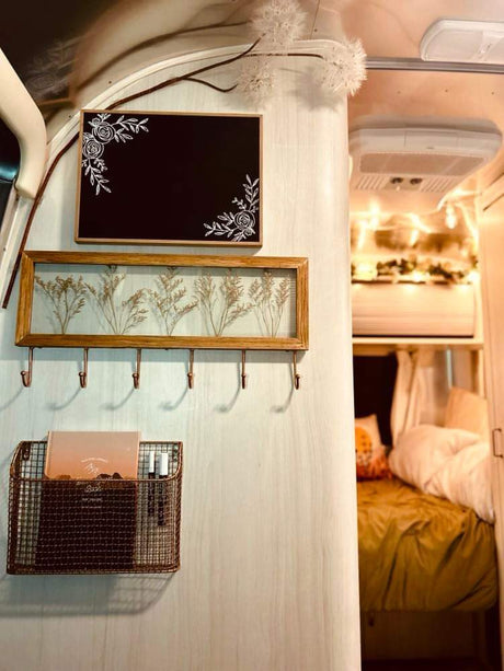 This RV rental interior features decorative signs, a pressed botanical frame with hooks, and a mesh basket, leading to the cozy bedroom.
