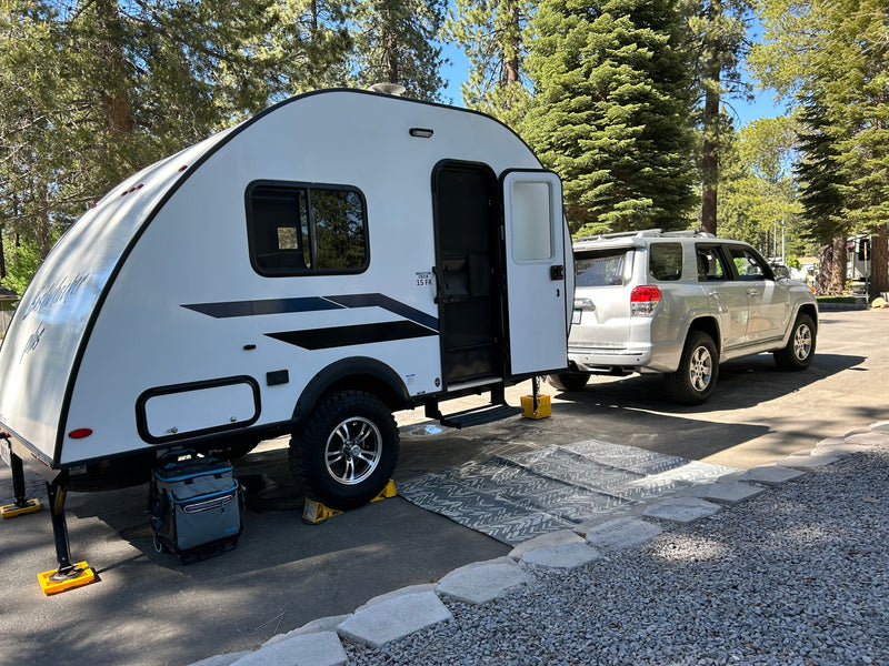White Braxton Creek travel trailer & silver SUV set up at a wooded campsite for an rv rental getaway.|A silver SUV tows a compact travel trailer RV rental through a snowy pine campground — photo 1