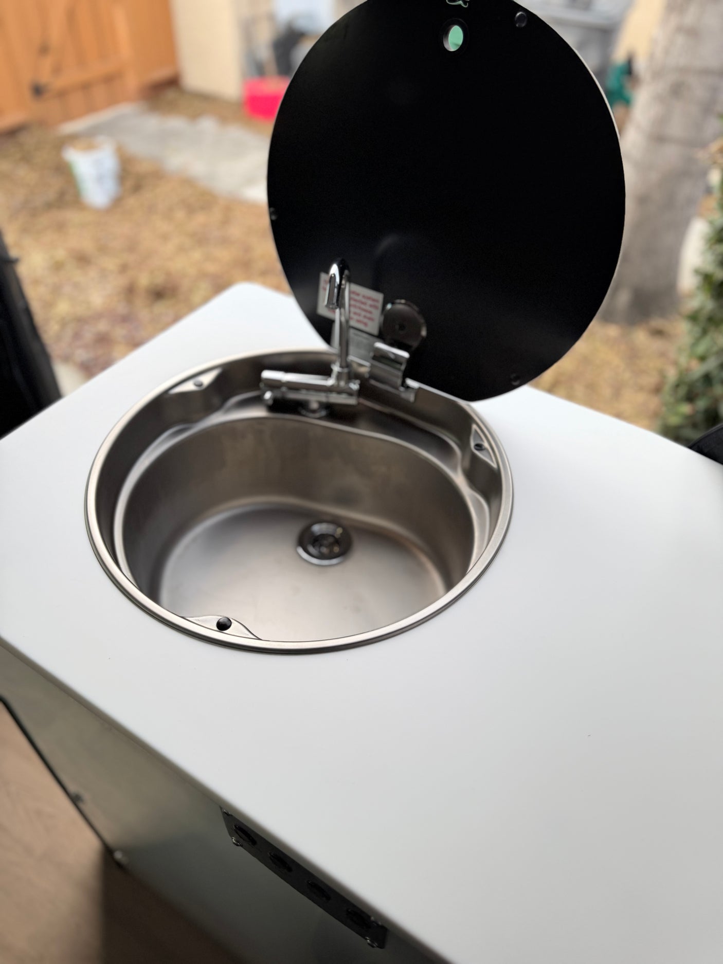 This RV rental features a compact stainless steel sink with a faucet and an open black lid, perfect for outdoor use.