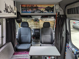 RV rental interior: Features front seats, table, privacy curtains, and scenic overhead art. Ideal for road trip adventures.