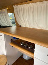 This RV rental features a bright wood interior with white gathered curtains & built-in mounted bowls, seen from above. Perfect for road trips!