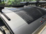 Top view of an RV rental roof showing a wet flexible solar panel, roof racks, and a vent.