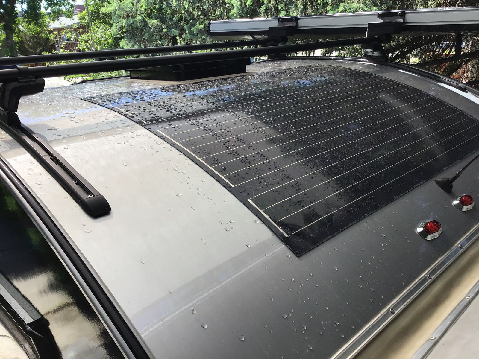 Top view of an RV rental roof showing a wet flexible solar panel, roof racks, and a vent.