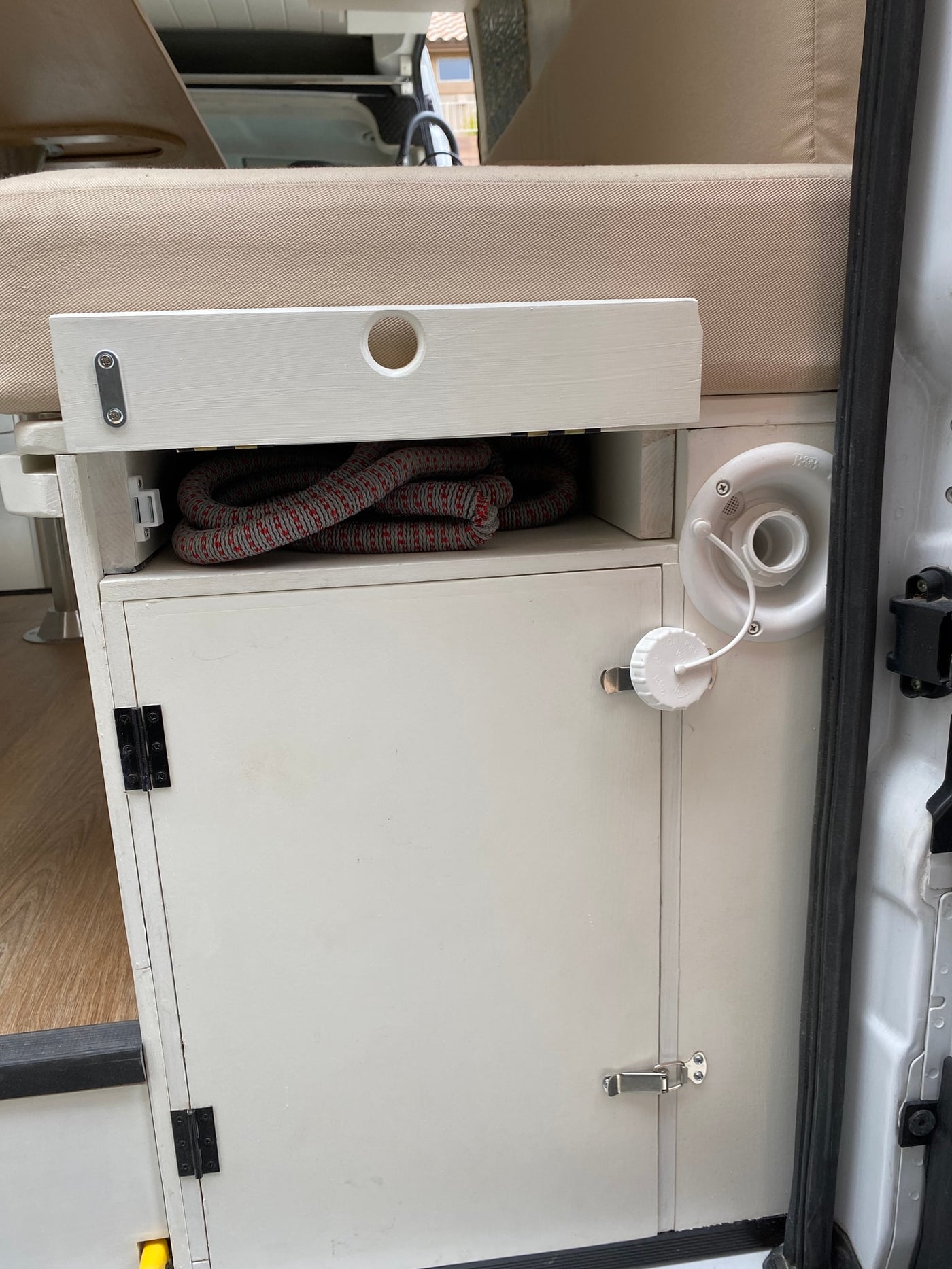 RV rental interior showing a white utility cabinet with water fill port, organized rope storage, and cushioned seating. — photo 20