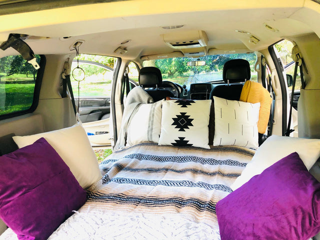 Cozy interior of an RV rental, featuring a comfortable bed with decorative pillows & striped blankets, ideal for car camping.