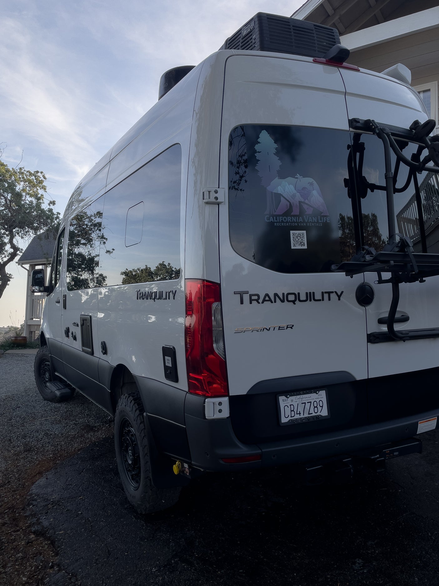 White Mercedes Sprinter RV rental van, "Tranquility," with a bike rack & "California Van Life" decal.
