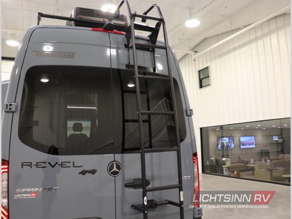 Rear of a grey Winnebago Revel Sprinter RV with roof rack & ladder, excellent for rv rental, shown at a dealership.