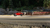 Red Jeep towing a compact RV rental camper on a highway, ideal for outdoor travel.