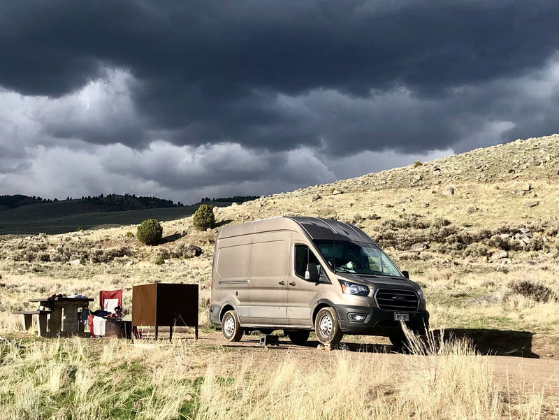 RV rental: A tan camper van parked on a dirt road with a picnic setup — photo 1