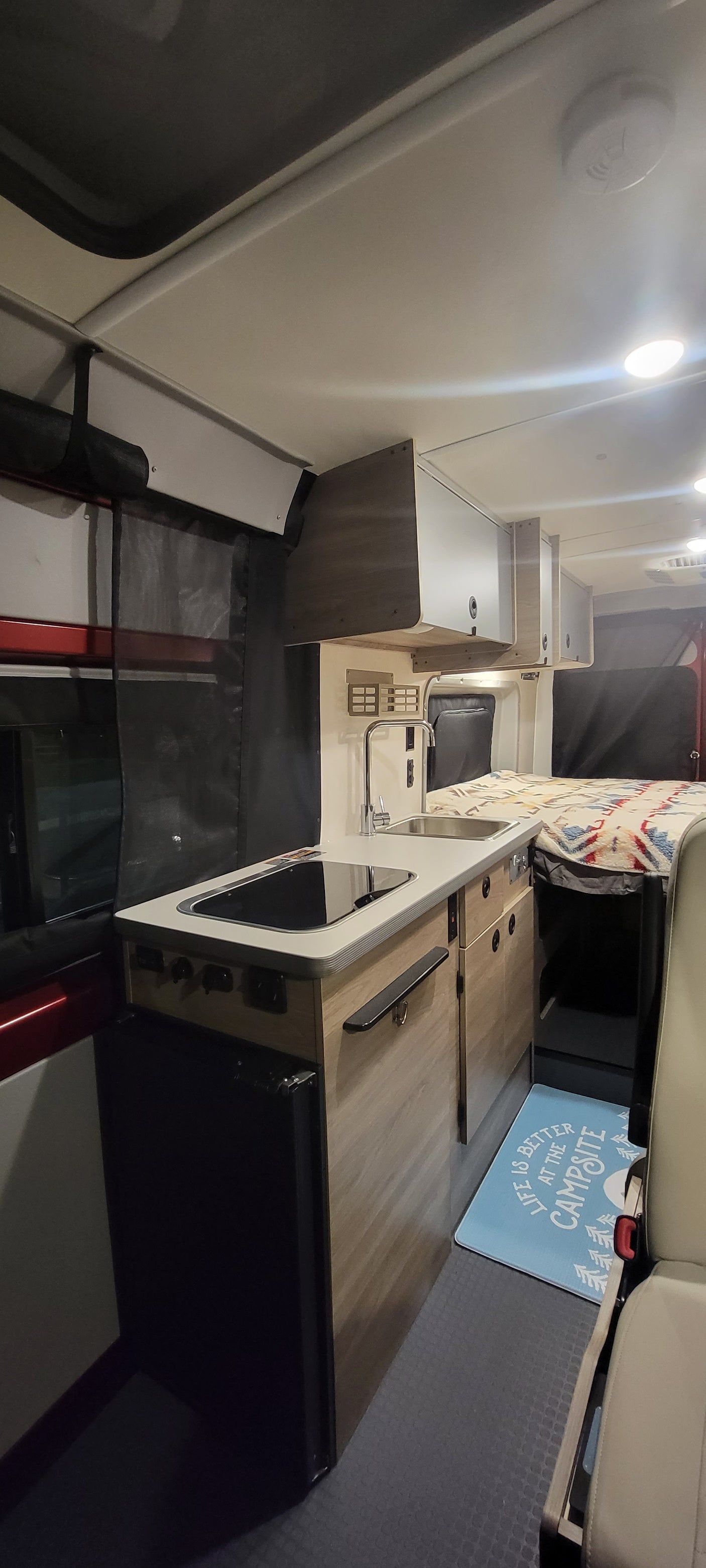 Inside this modern RV rental: a compact kitchen with sink, cozy sleeping area, overhead lighting, and ample storage.