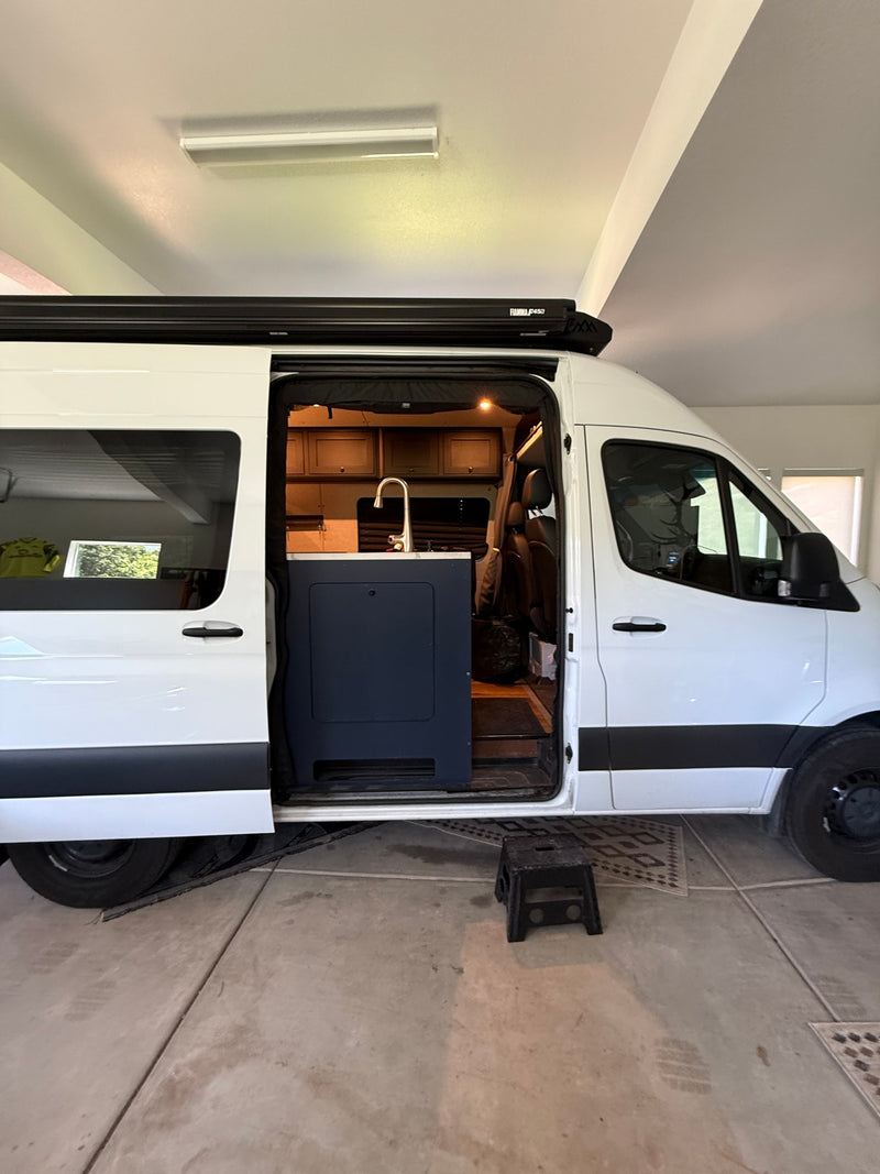 White RV rental camper van with open side door showcasing its fitted interior, including a kitchen sink and overhead cabinets. — photo 12