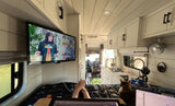 A person relaxes in a cozy rv rental, feet up on a laptop, watching TV with their cat in this compact, pet-friendly mobile home.
