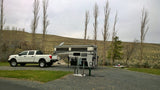 White truck with detached truck camper at an RV site, ready for an RV rental outdoor adventure among bare trees and hills.