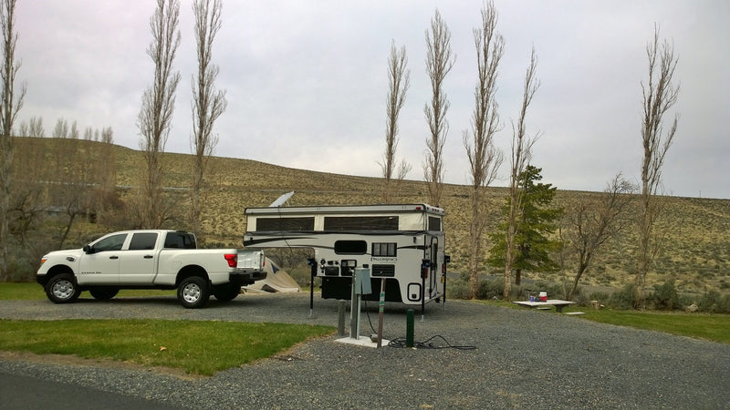  and a set dining table with flowers on green grass under trees.|A white truck with a Palomino RV rental and two bicycles on a rack — photo 3