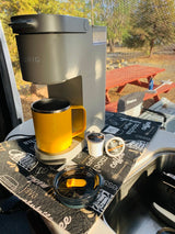 Enjoying fresh coffee in an RV rental. A Keurig brewer with a yellow travel mug and Peet's K-cups sits on a coffee mat.