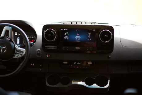 Inside a Mercedes-Benz RV rental: a modern dashboard with navigation on the infotainment screen, steering wheel, and controls.